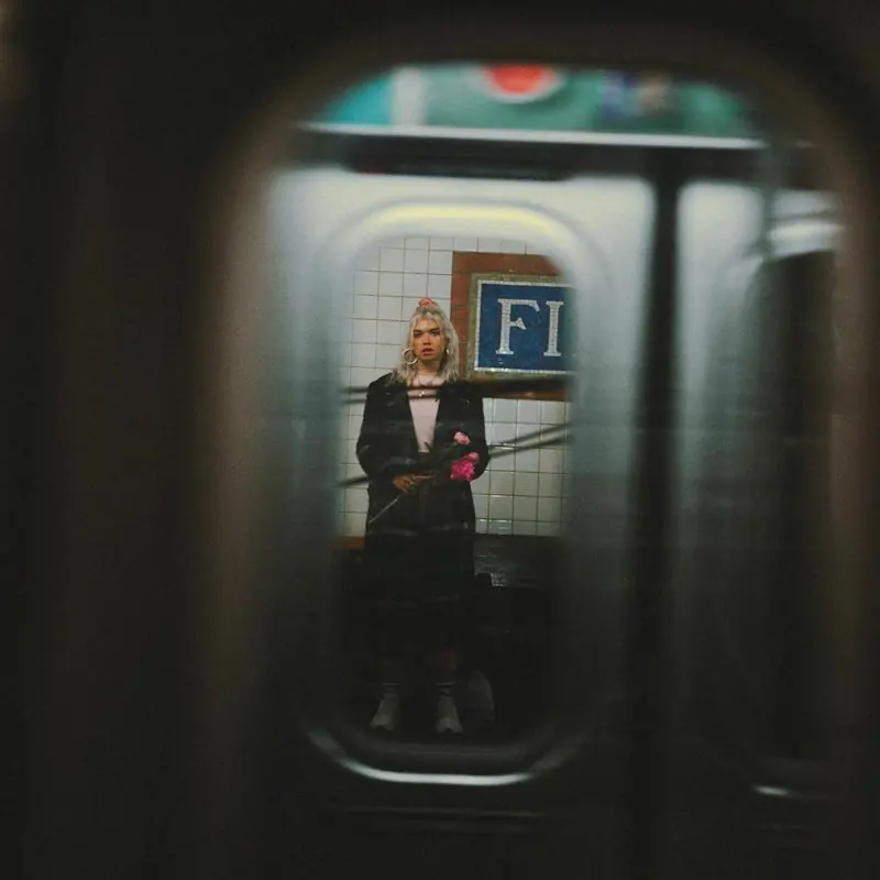 A person holding pink flowers on a metro platform, framed by a train window.